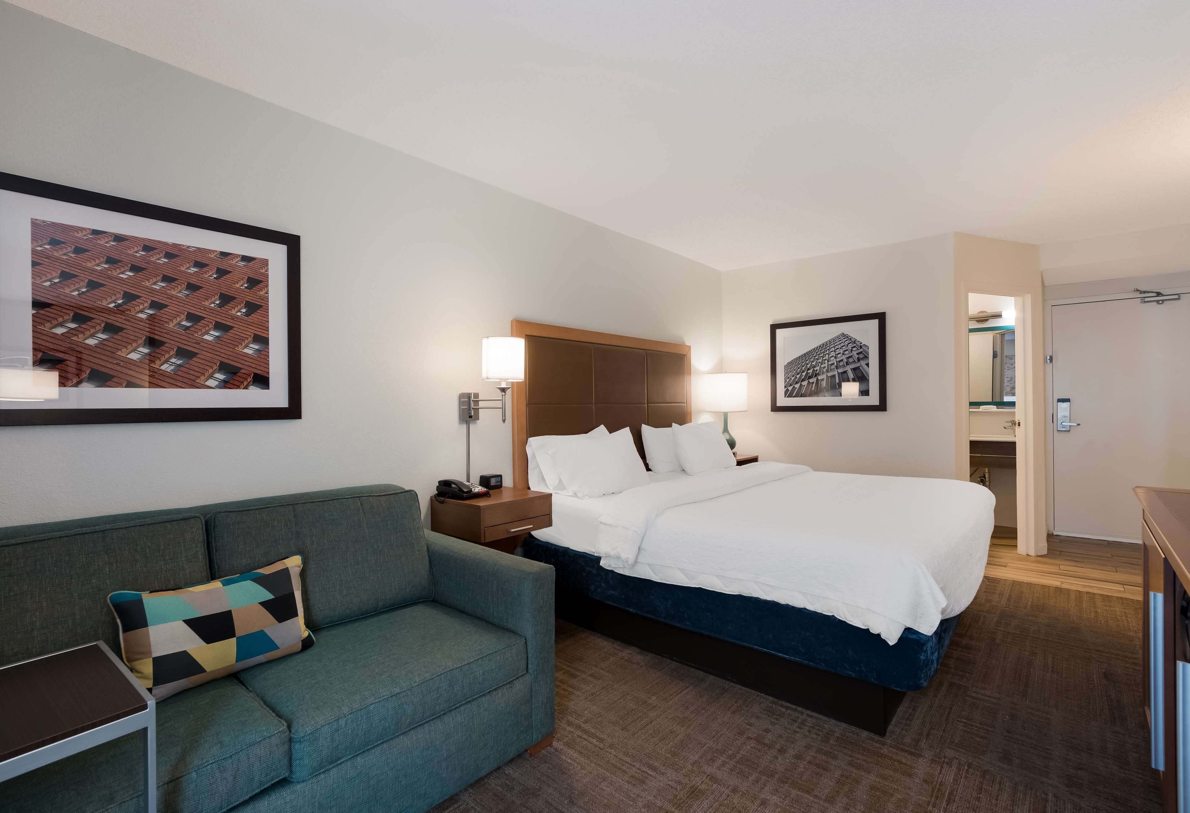 A hotel room with a bed, a sofa, a nightstand, and a wall-mounted lamp.