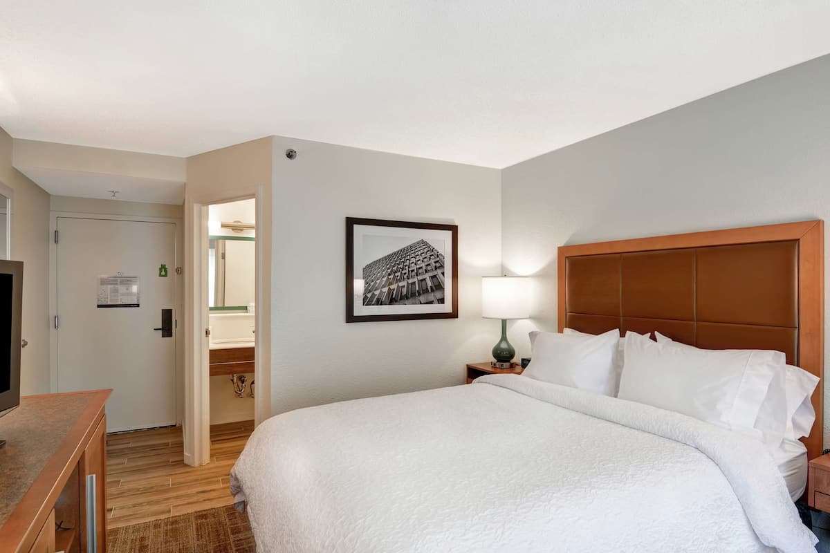 A hotel room with a large bed, a television on a wooden table, a framed picture on the wall, and a door leading to a bathroom.