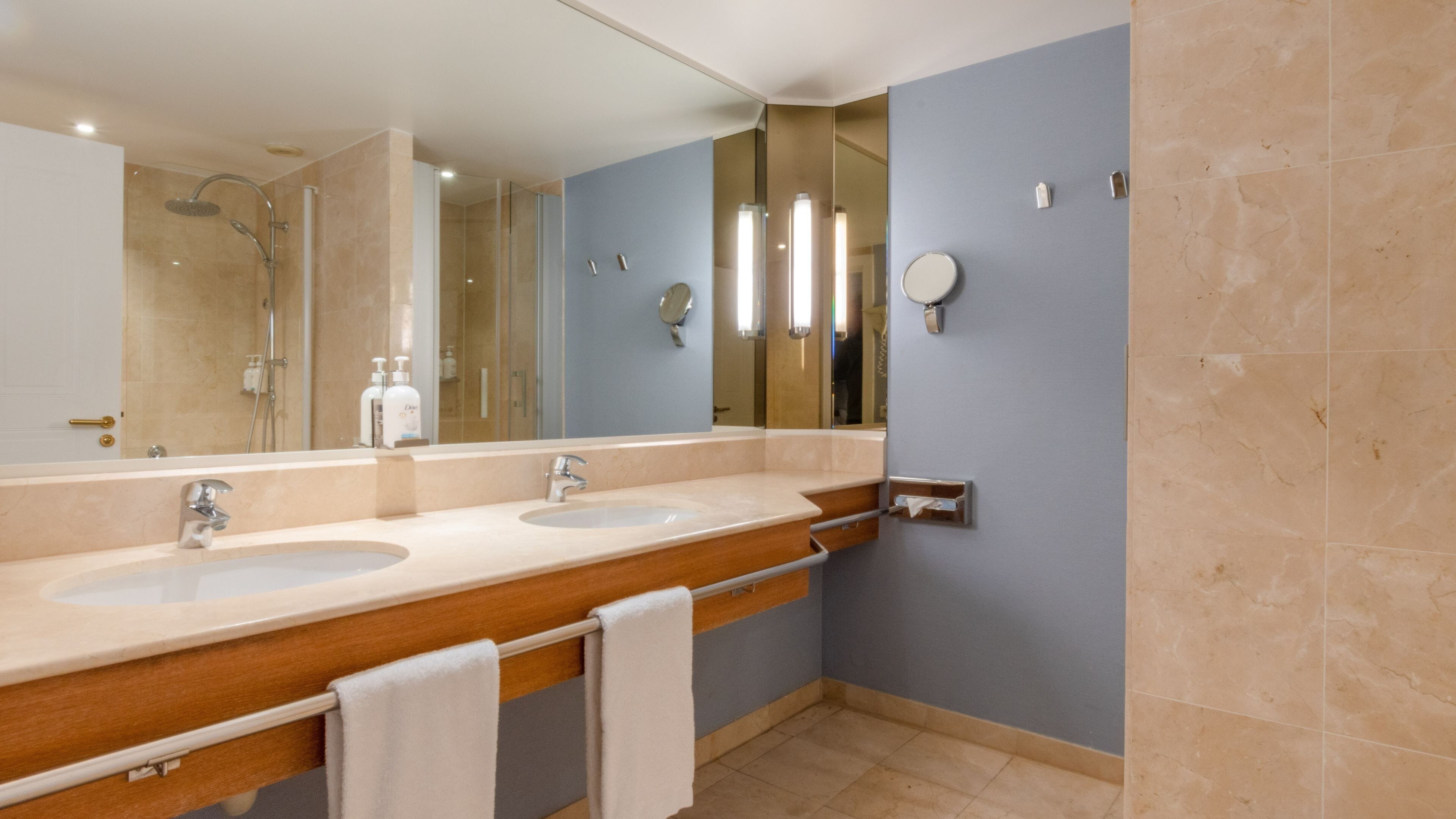 A modern bathroom with two sinks, a shower, and a large mirror.