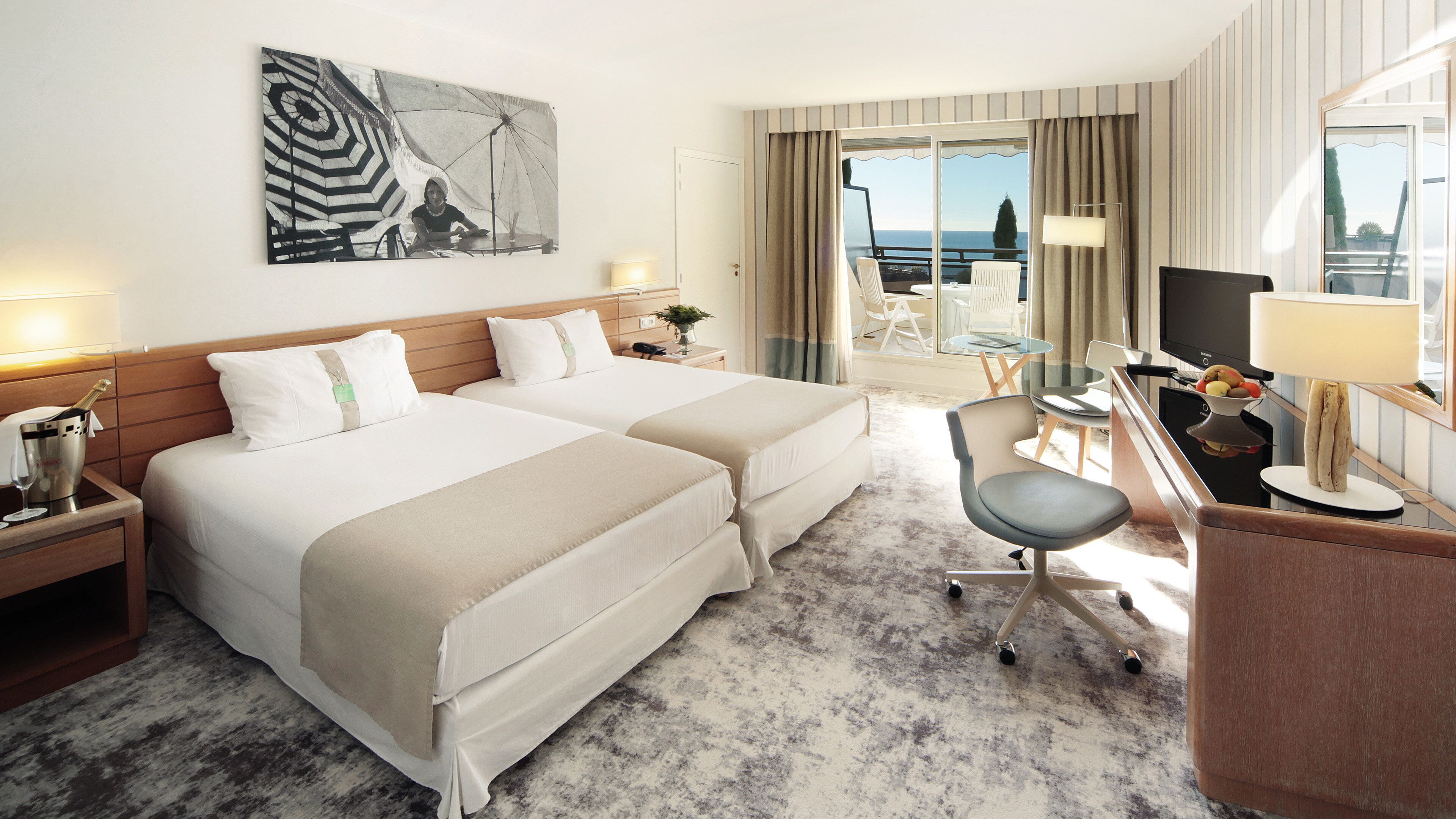 Ein Hotelzimmer mit zwei Betten, einem Schreibtisch mit Stuhl, einem Fernseher und Meerblick.