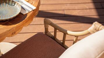 Une terrasse en bois avec une chaise en osier et une table sur laquelle se trouvent une assiette, une serviette et des couverts.