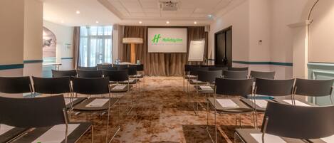 A conference room with rows of chairs, a projector screen, and a banner for Holiday Inn.