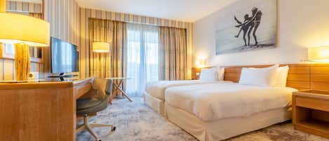 A hotel room with a large bed, a desk with a chair, a TV, and a painting on the wall.