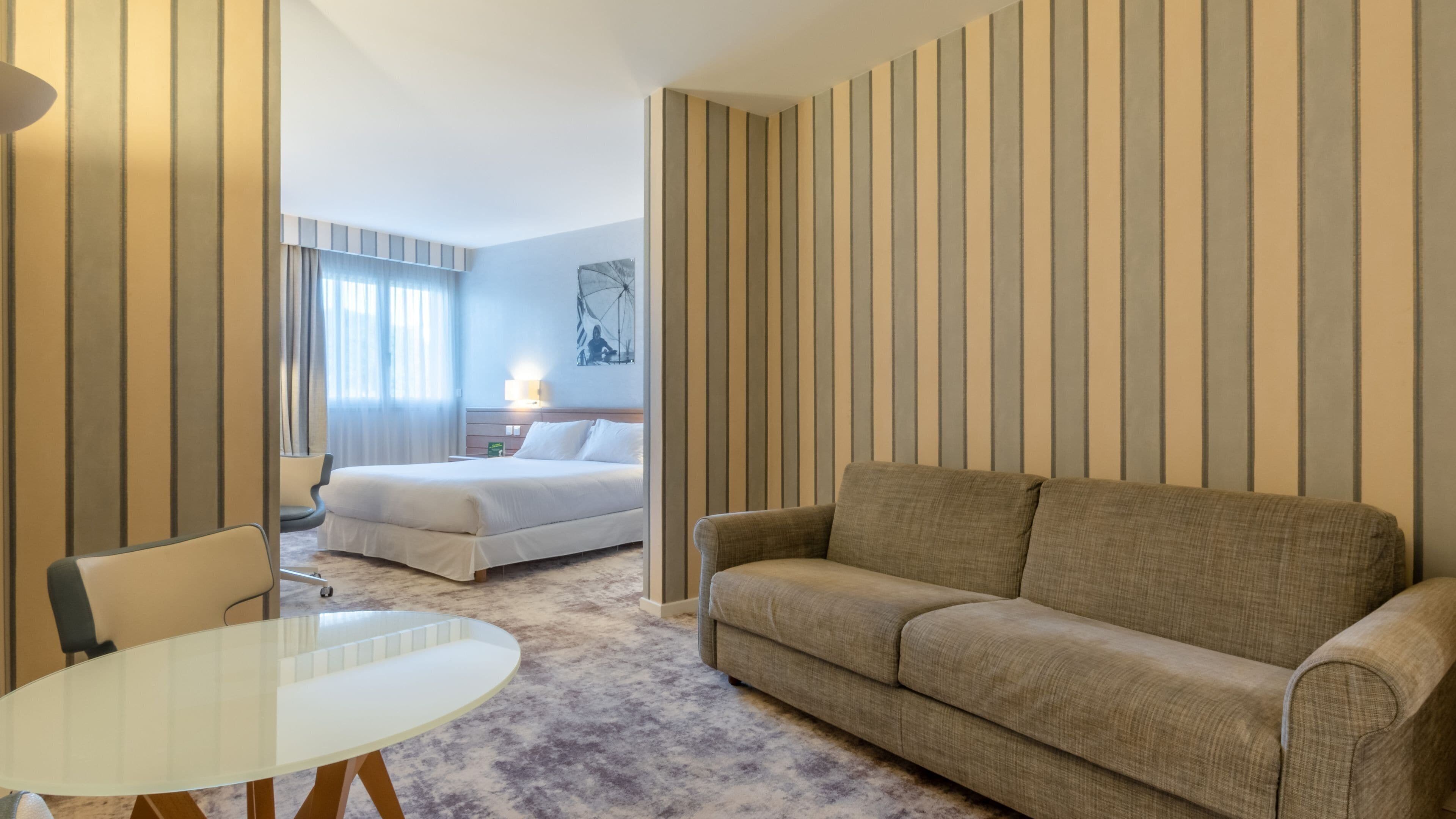 Ein Hotelzimmer mit einem Bett, einer Couch, einem Glastisch und rautenmusterter Tapete.
