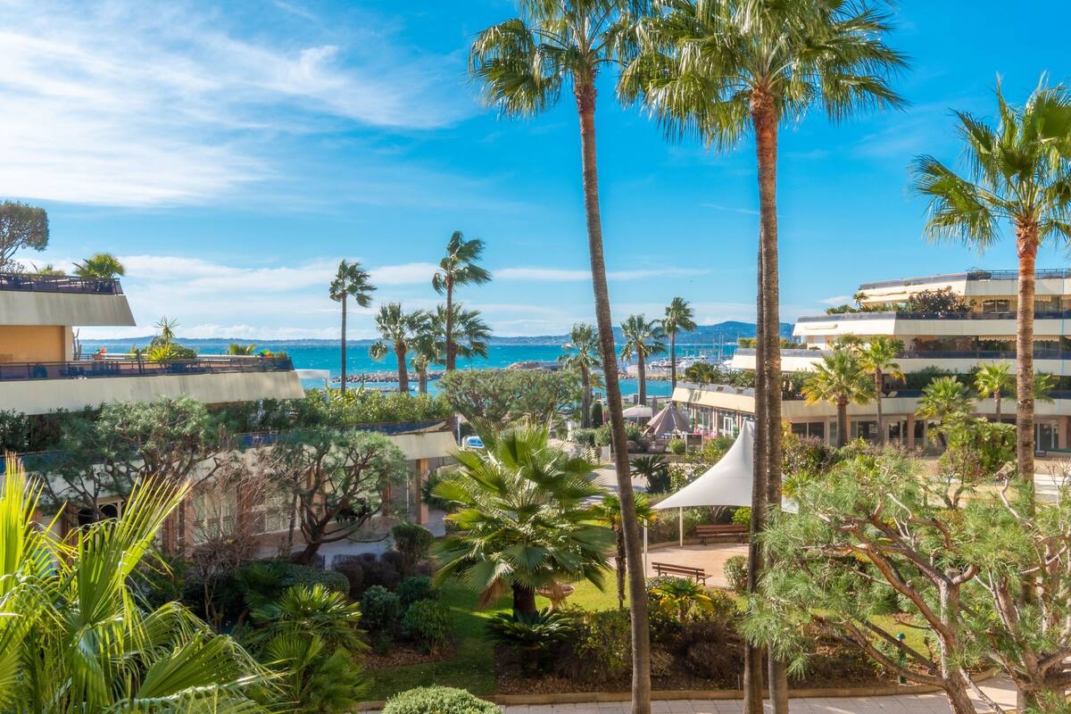 A resort with multiple-story buildings, palm trees, and a view of the sea.