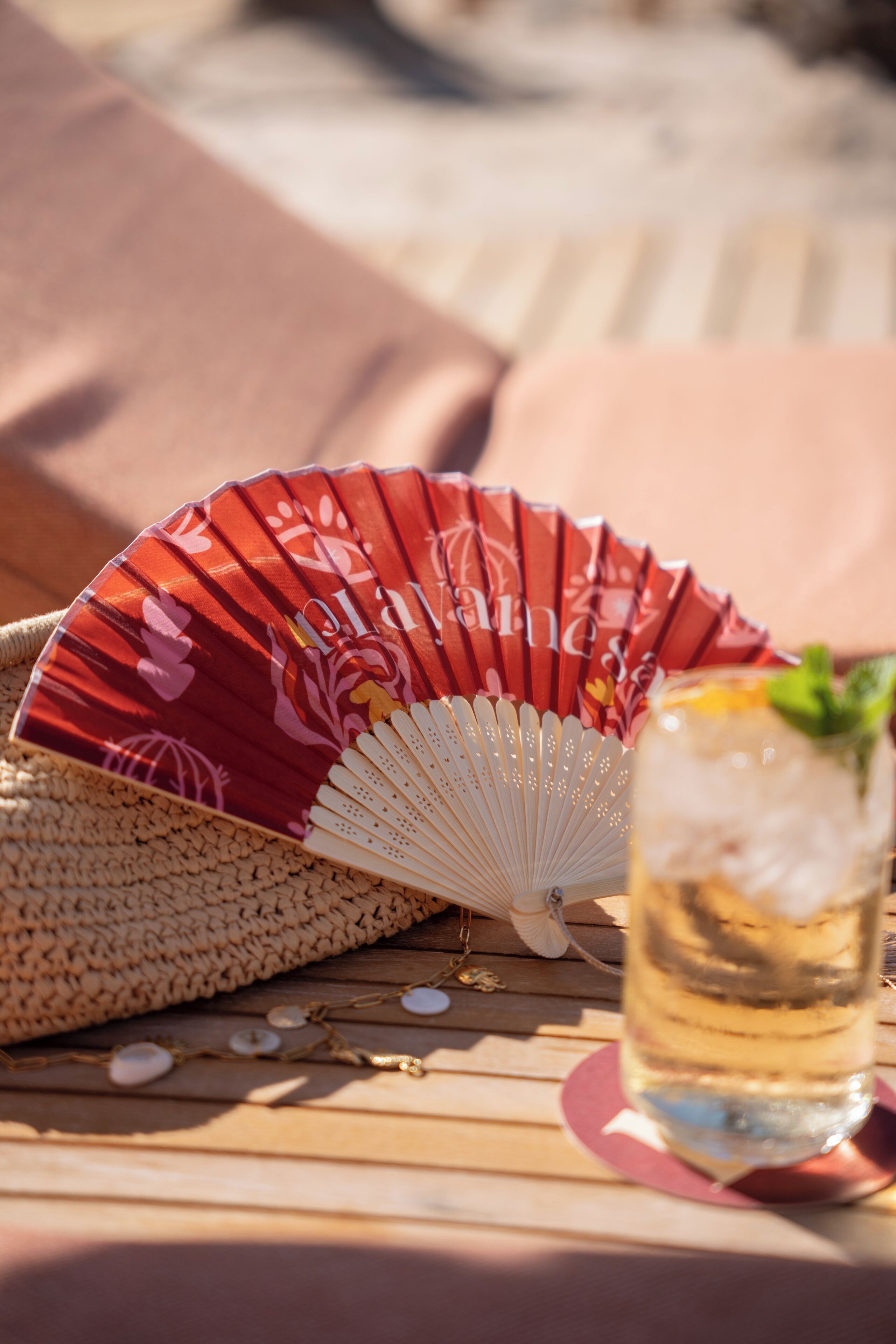 A fan, a glass with a mint garnish, and a woven basket on a wooden surface.