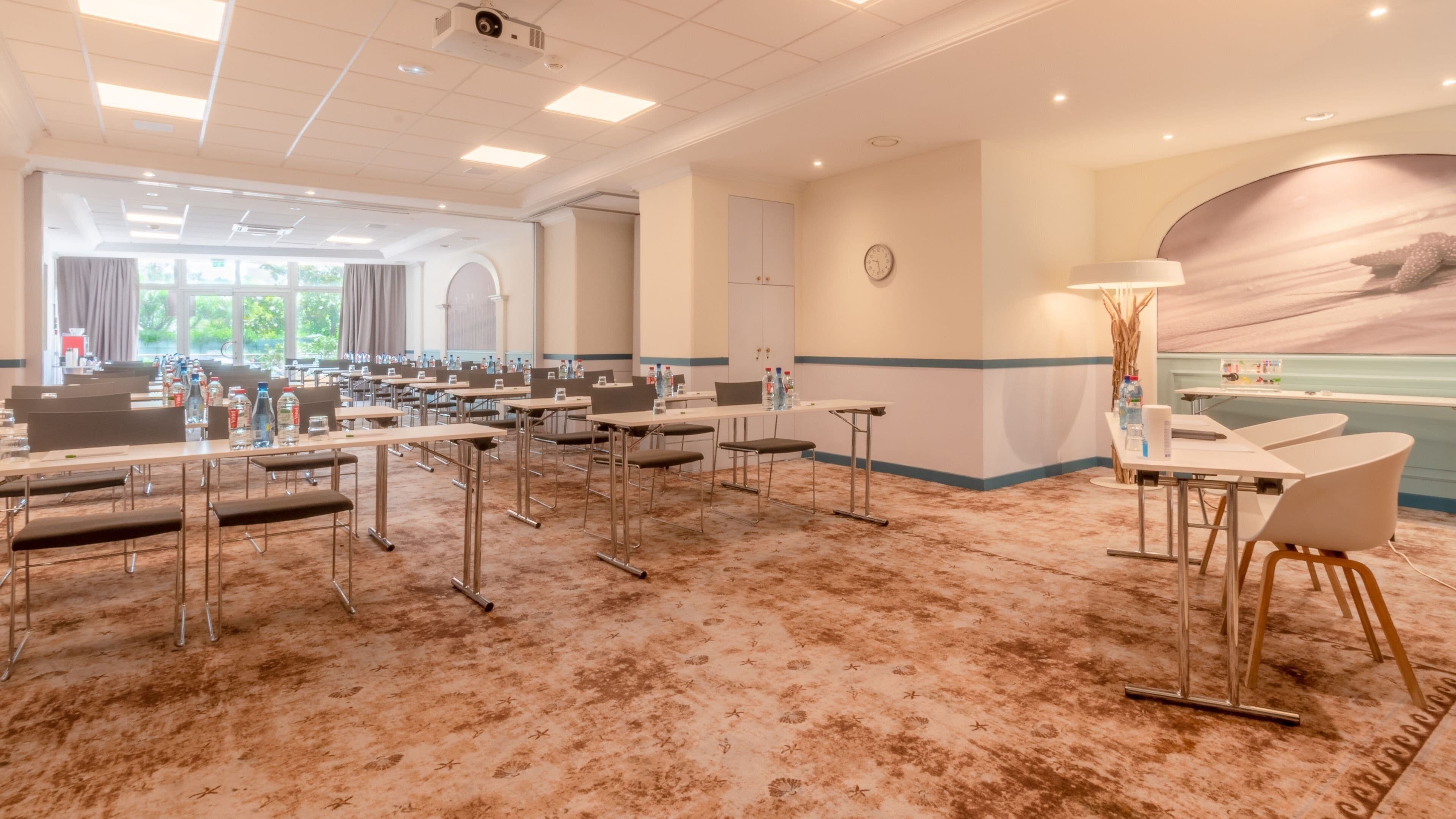 A conference room with multiple tables and chairs, a clock on the wall, and a large window with curtains.