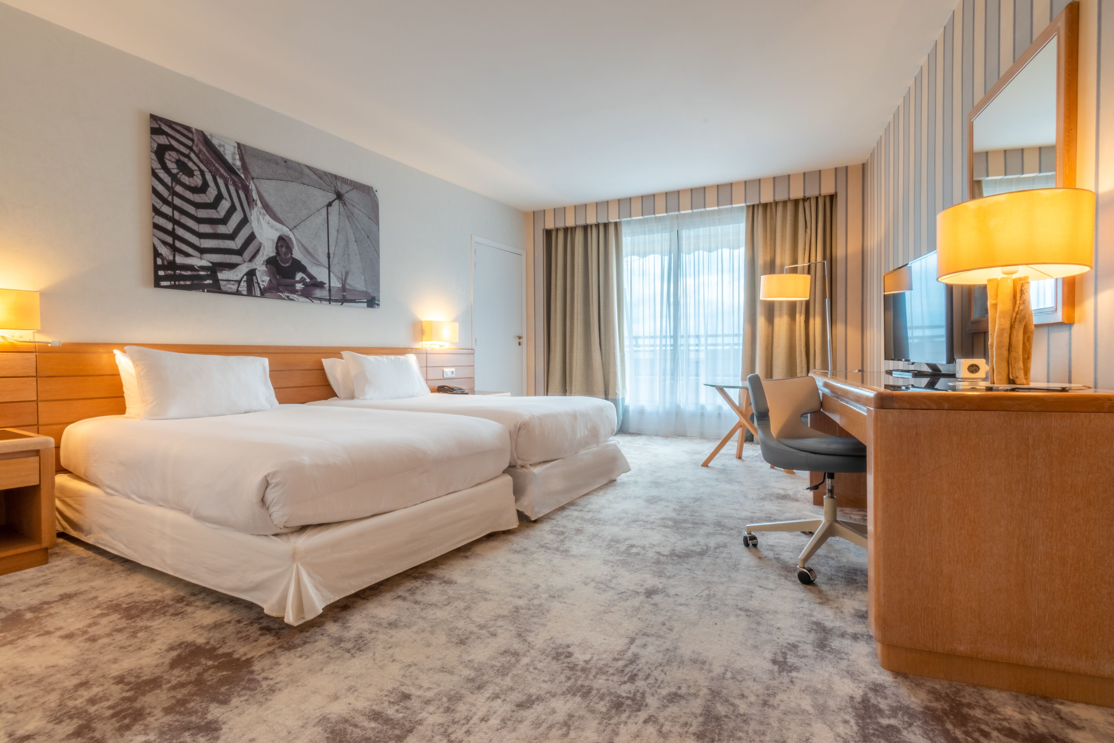 A hotel room with a large bed, a desk, a chair, and a desk lamp.