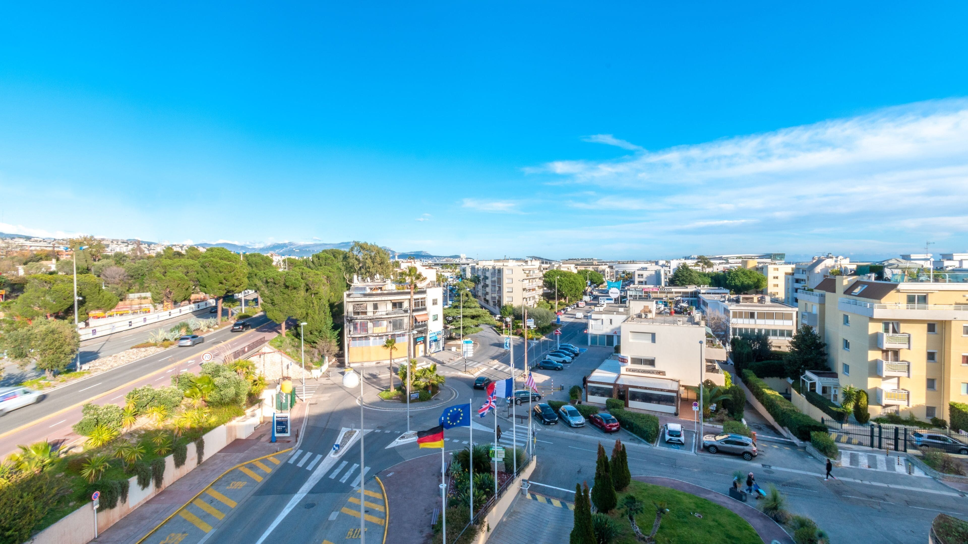 A cityscape with a clear blue sky, a road with cars, and buildings with balconies.