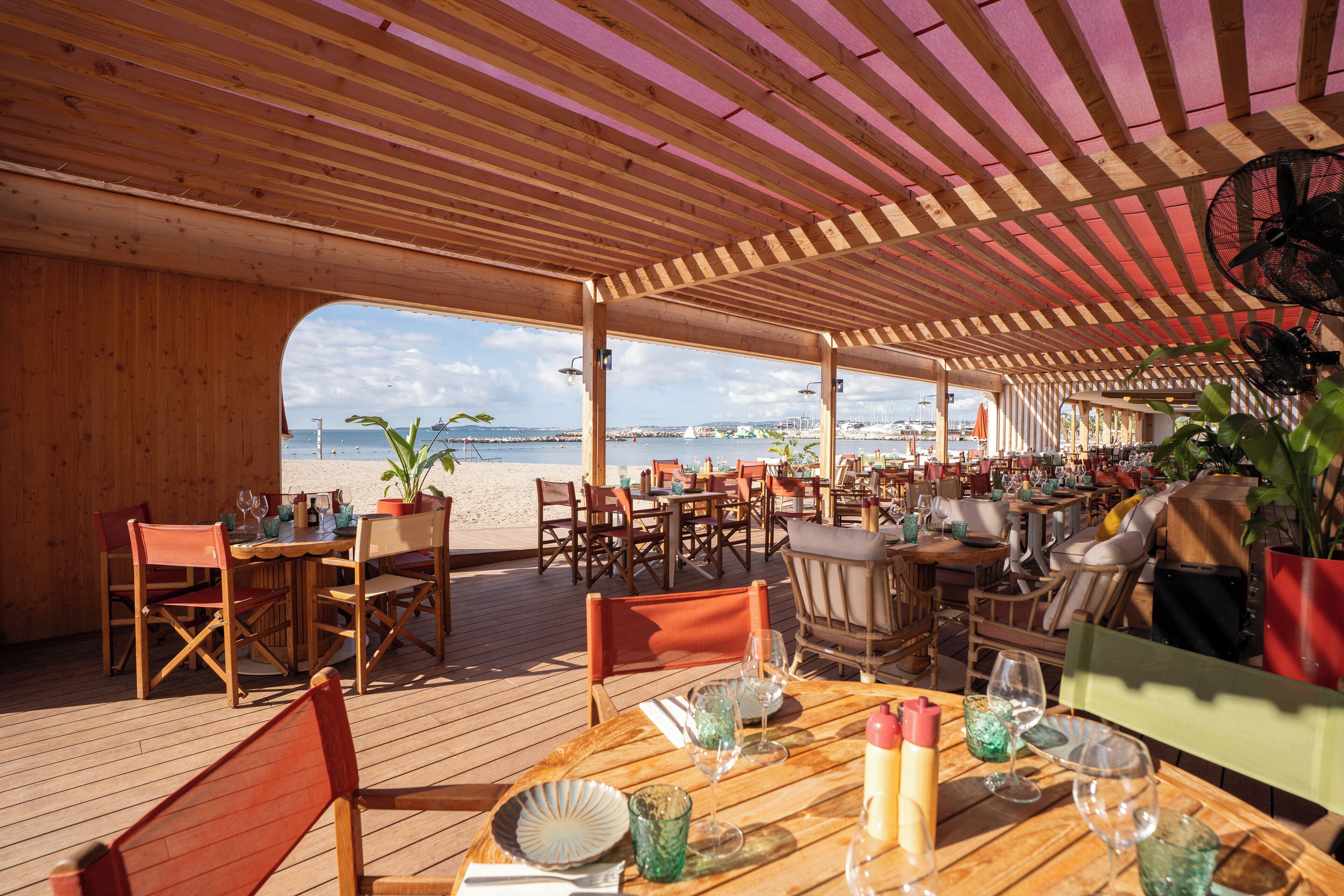 An outdoor dining area with wooden tables and chairs, overlooking a beach.