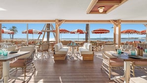 An outdoor seating area with tables, chairs, and umbrellas overlooking the beach. - Holiday Inn Nice-Port St Laurent by IHG (Saint-Laurent-du-Var)