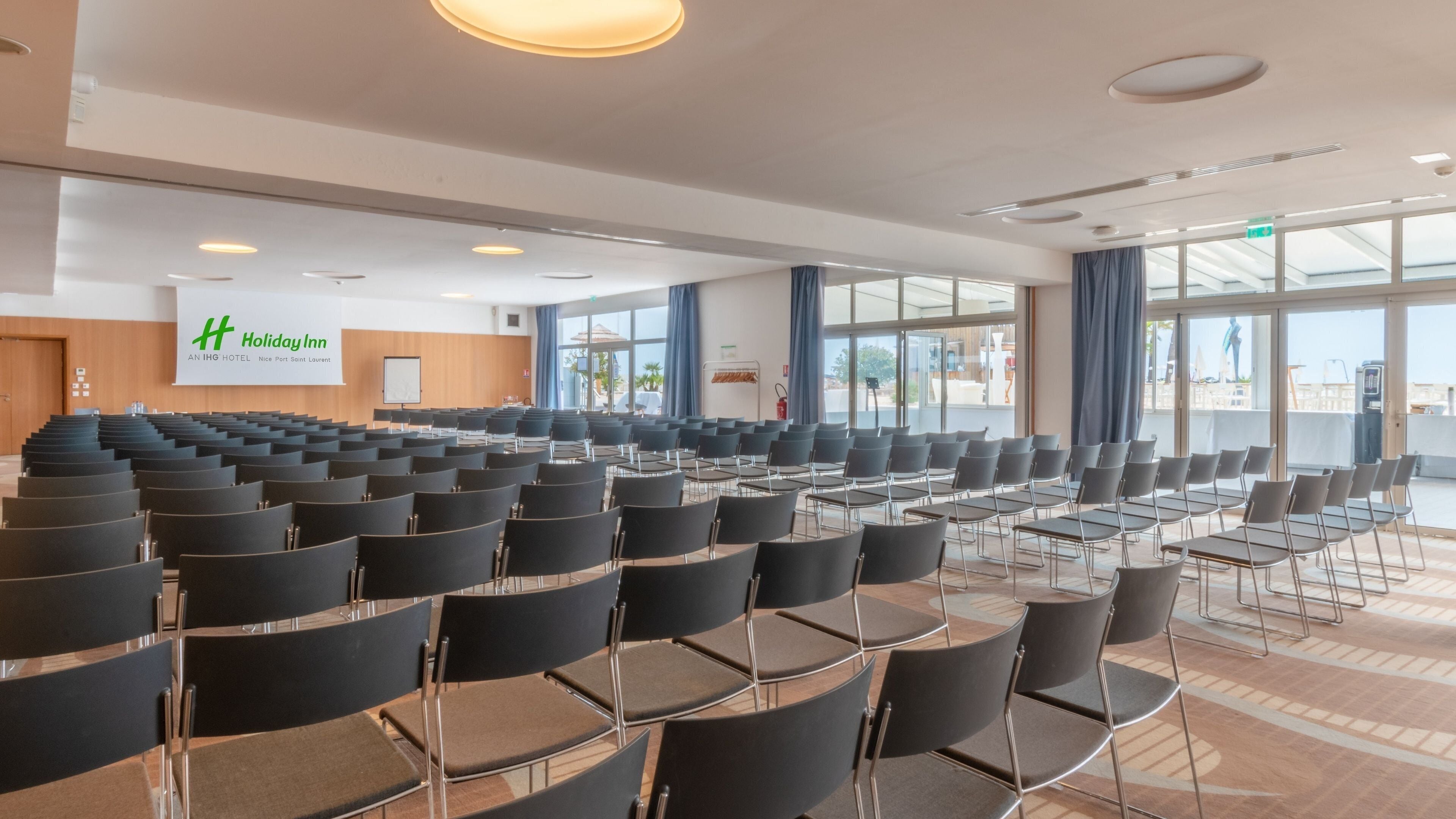 A conference room with rows of chairs, a large screen, and a banner for Holiday Inn.
