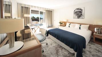 Ein Hotelzimmer mit einem Bett, einem Schreibtisch mit Lampe, einem Stuhl, einem kleinen Tisch und einem Fenster mit Vorhängen.