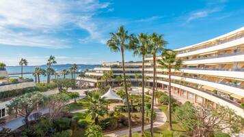 Un hotel de varios pisos con un patio central, palmeras y vista al mar.