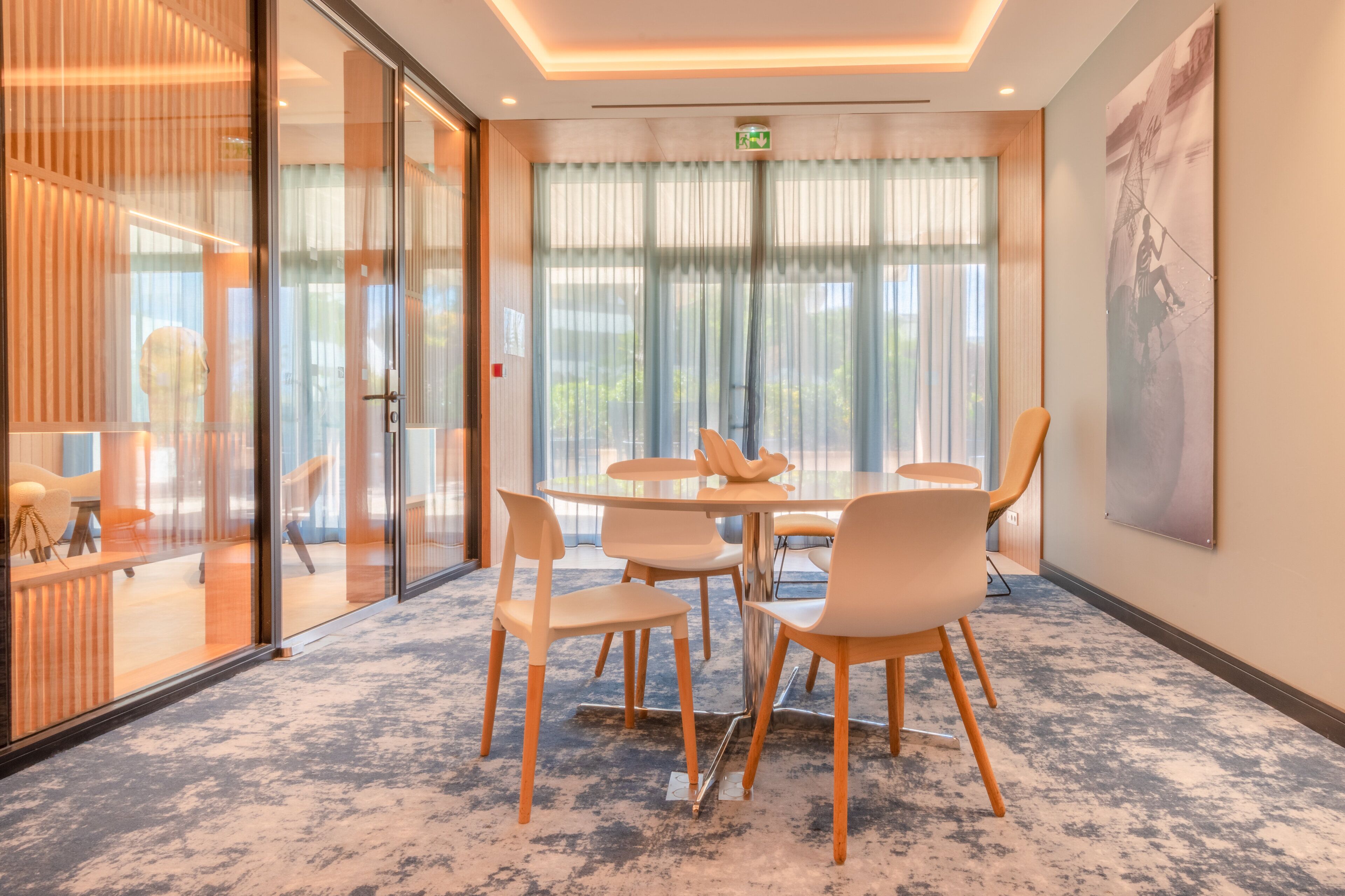 A modern conference room with a round table, six chairs, and a large window with sheer curtains.