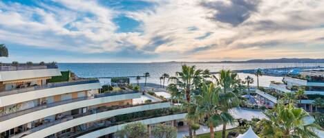 A coastal hotel with multiple balconies overlooking the sea, palm trees, and a modern architectural design.