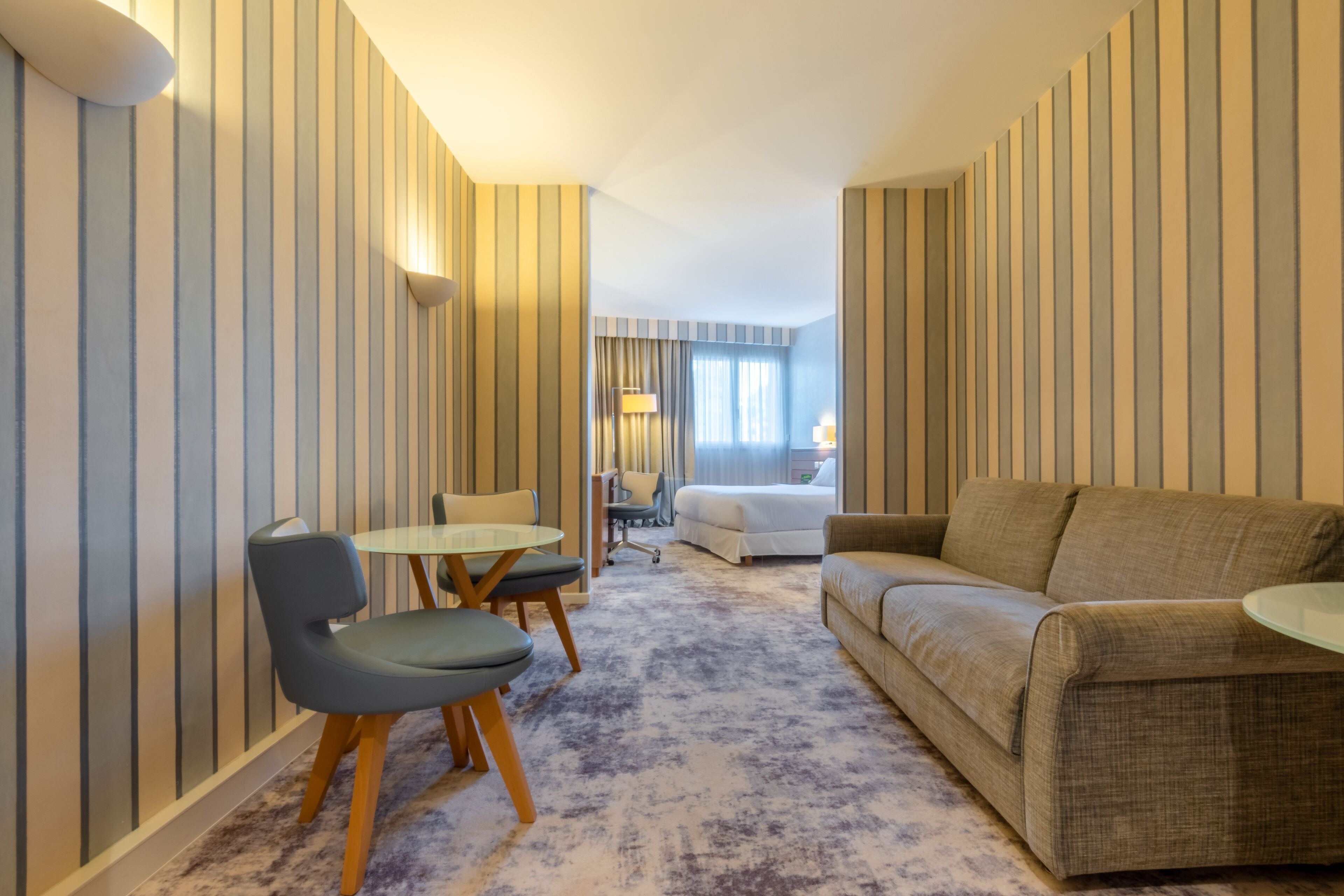 Une chambre d’hôtel avec un mur à rayures, un lit, un canapé, une petite table et une chaise.