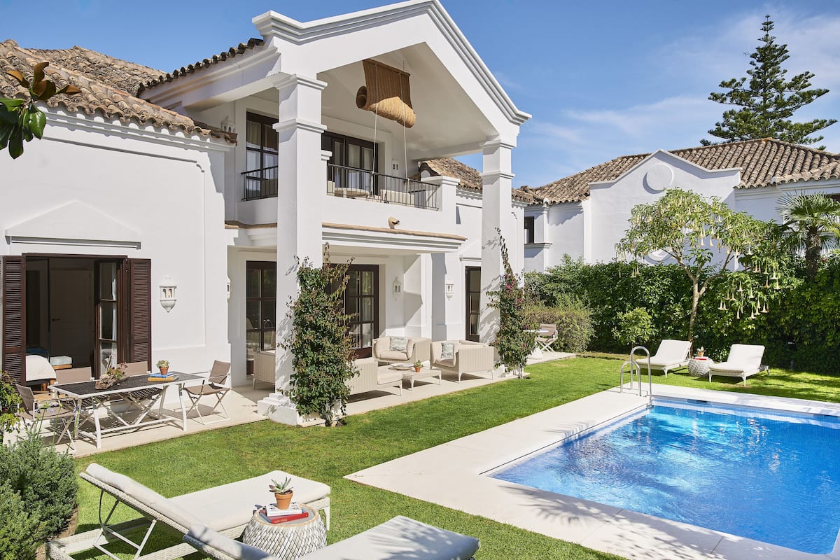 A two-story house with a swimming pool, outdoor seating, and a well-maintained lawn.