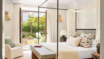A bedroom with a four-poster bed, a bedside table, a chair, and a view of the garden through a glass door.