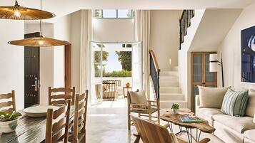 A spacious living area with a dining table, wooden chairs, a sofa, and a staircase leading to an upper level.