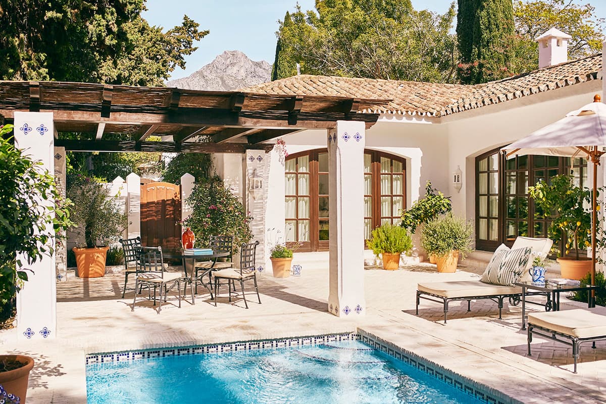 A poolside area with a pergola, outdoor seating, and potted plants.
