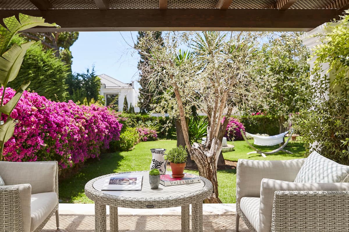 A covered outdoor seating area with wicker furniture, a small round table, and a potted plant.