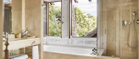 A modern bathroom with a large bathtub, a glass-enclosed shower, and a view of greenery outside.