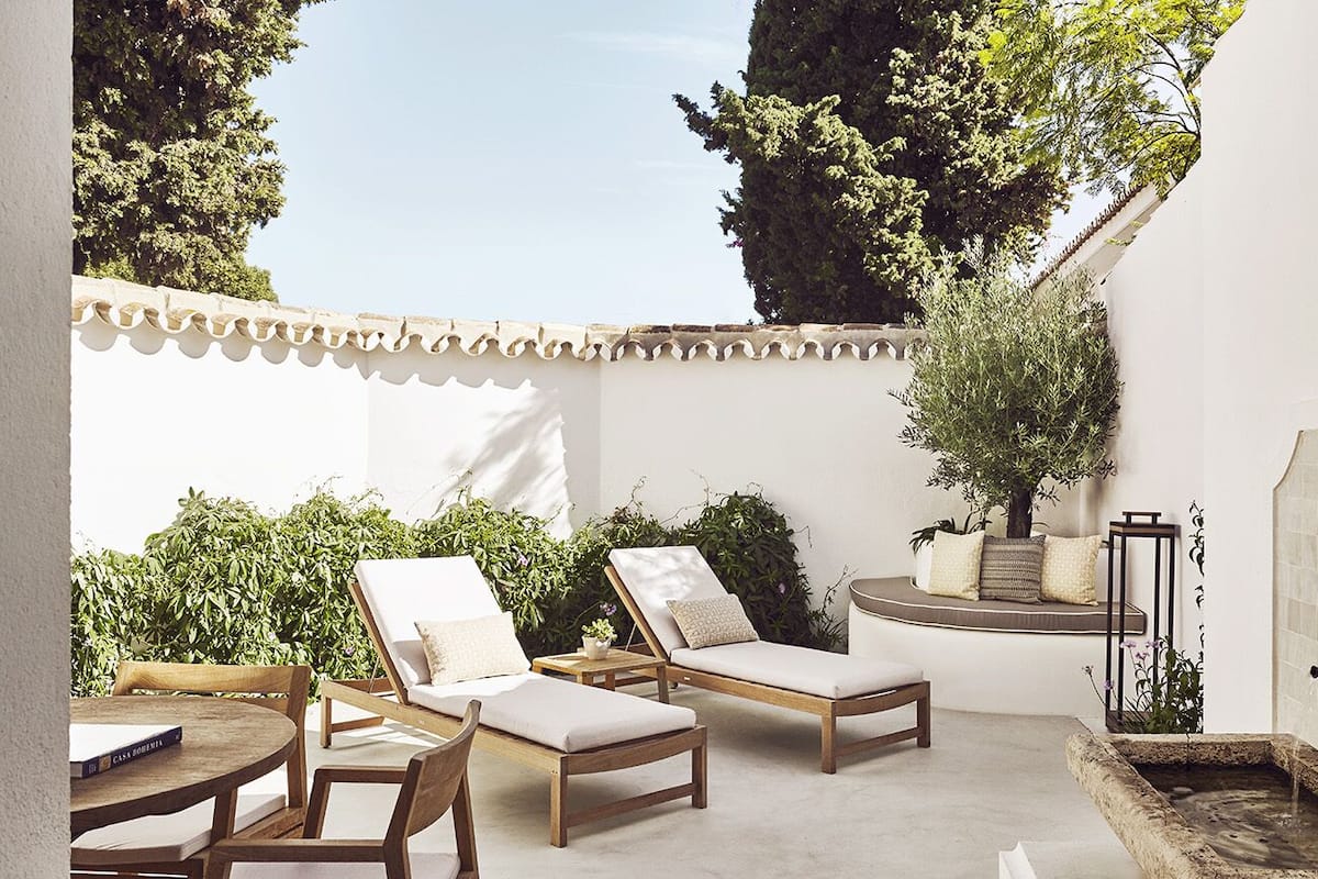 A sunlit patio with lounge chairs, a small table, and a tiled wall with a window seat.