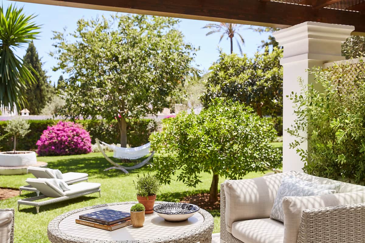 A sunlit outdoor seating area with a round table, lounge chairs, and a hammock.