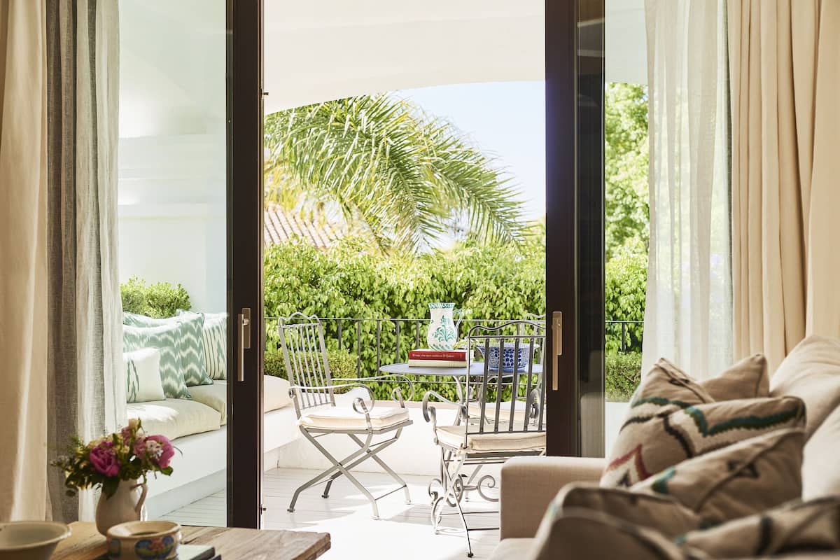 An open sliding glass door leading to a balcony with a sofa, a dining table, and chairs.