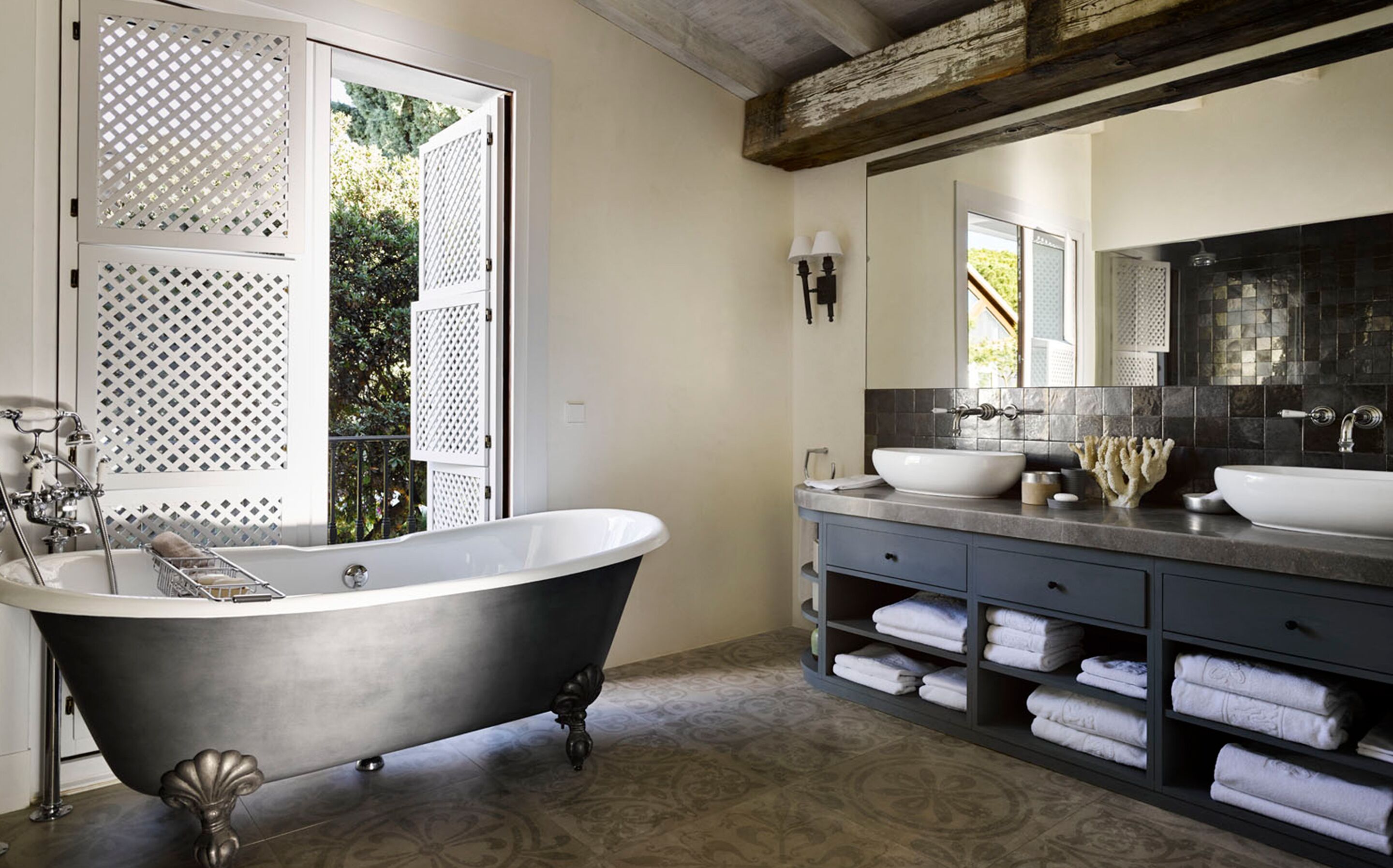 Une salle de bain avec une baignoire sur pieds, deux lavabos, un grand miroir et un porte-serviettes avec des serviettes pliées.