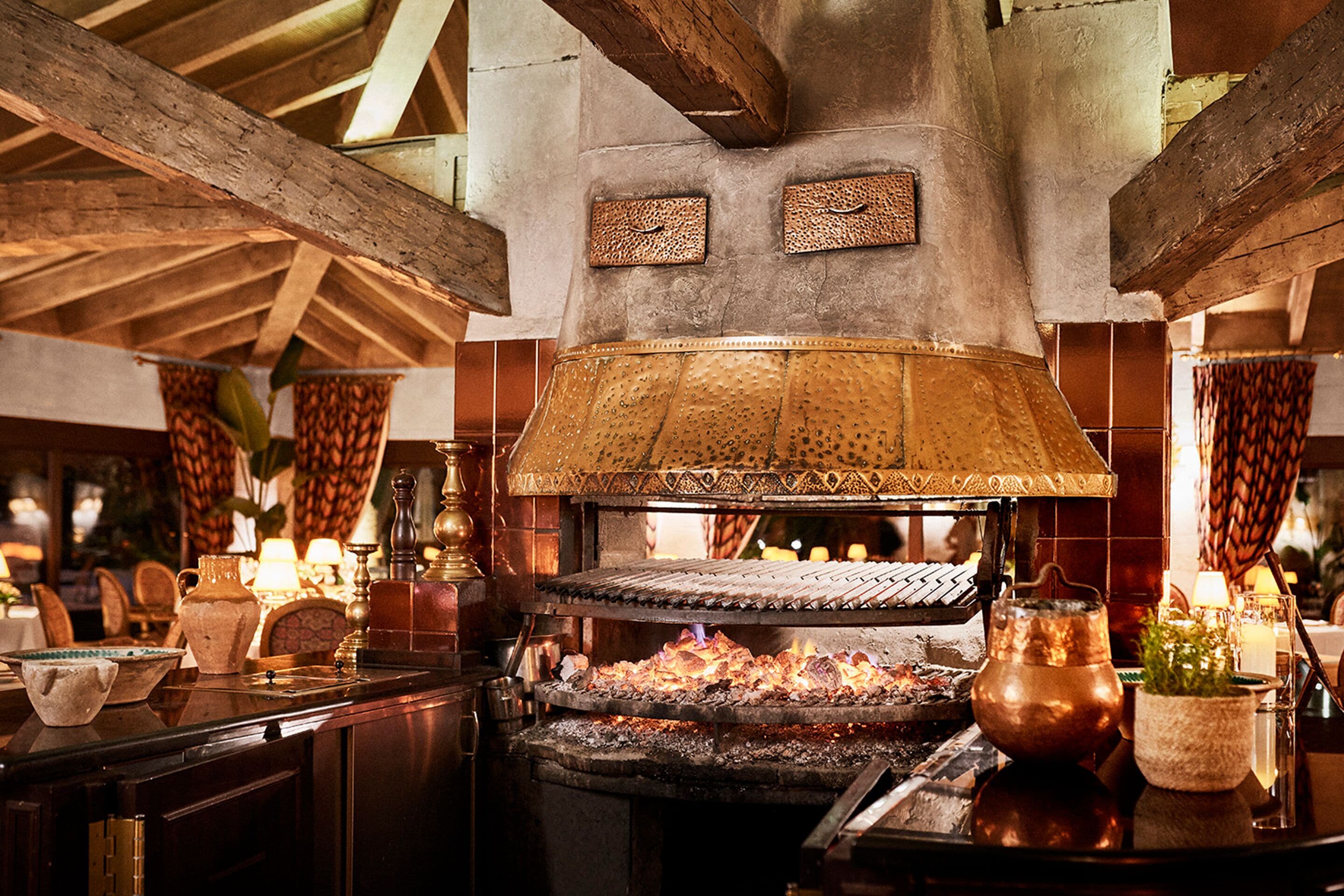 Un interior de restaurante con techo de vigas de madera, una olla de cobre grande y un horno de ladrillo.