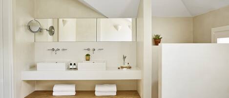 A modern bathroom with a large mirror, two sinks, and a wooden shelf with towels.