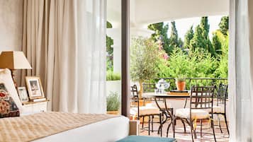 Et soveværelse med en seng, et sengebord med lampe, og udsigt til en udendørs balkon med stole og planter.