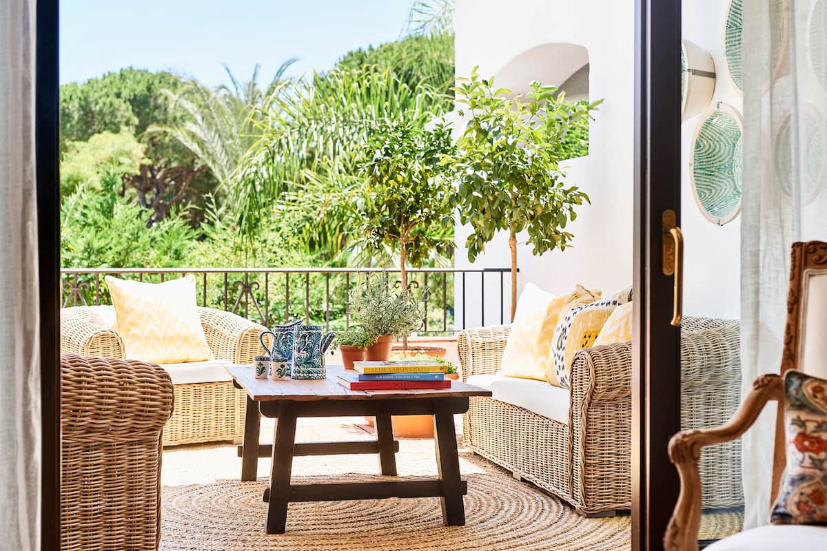 A balcony with wicker furniture, a potted plant, and a table with books.