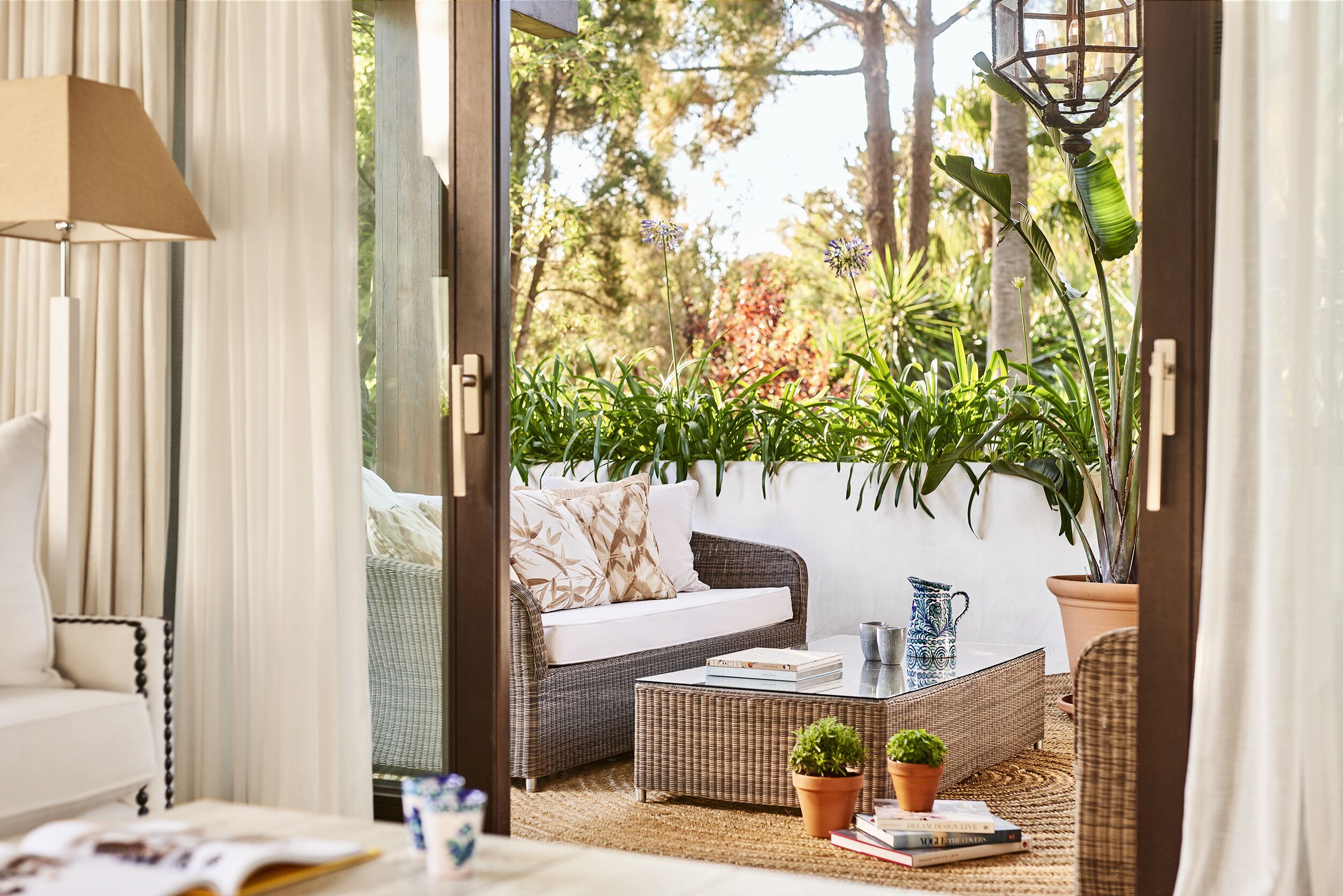 An open doorway to a patio area with wicker furniture, a table, and potted plants.