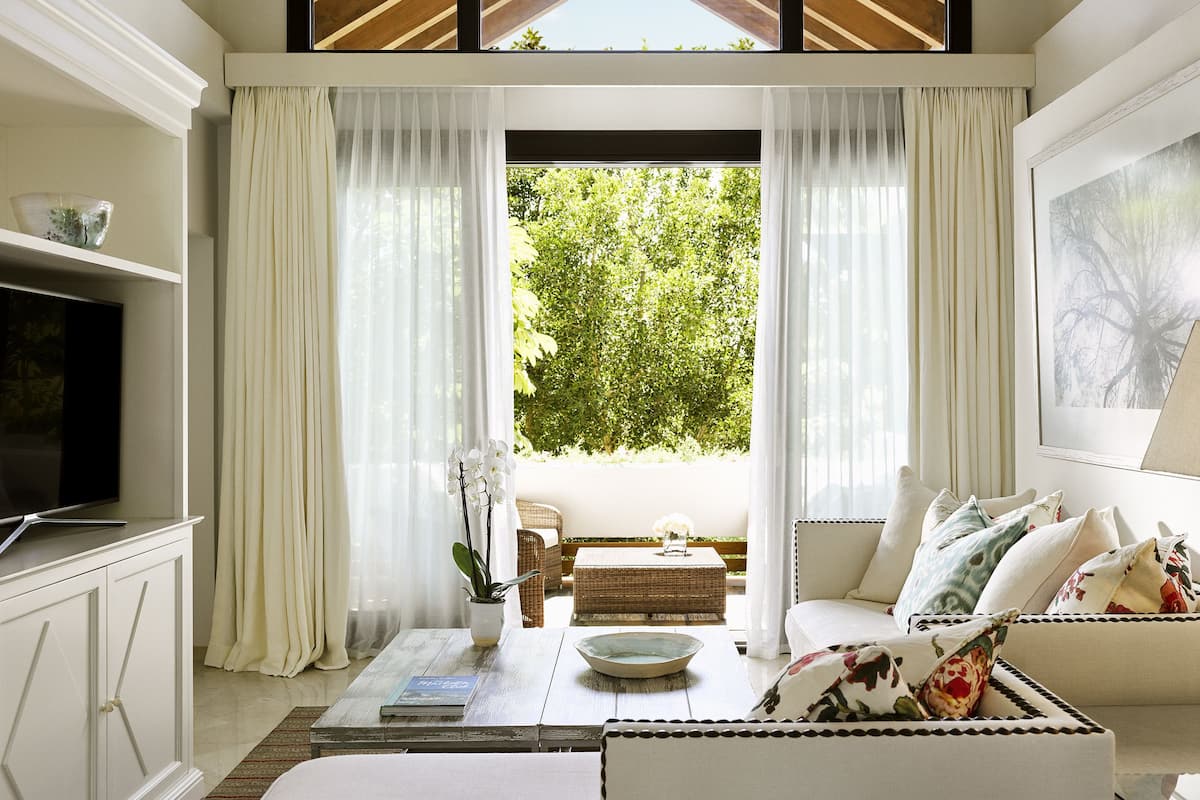 A modern living room with a television, sofa, and a view of greenery outside.
