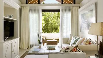 A modern living room with a television, sofa, and a view of greenery outside.