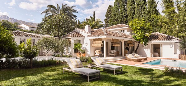 Una villa con piscina, mobiliario exterior y exuberante vegetación.