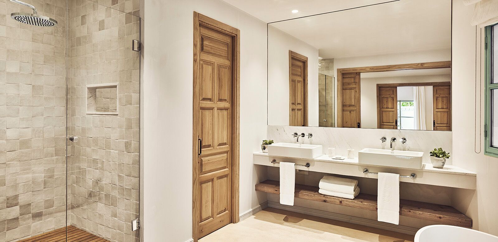 Une salle de bain moderne avec une douche à parois de verre, des portes en bois et un grand miroir au-dessus de deux vasques.