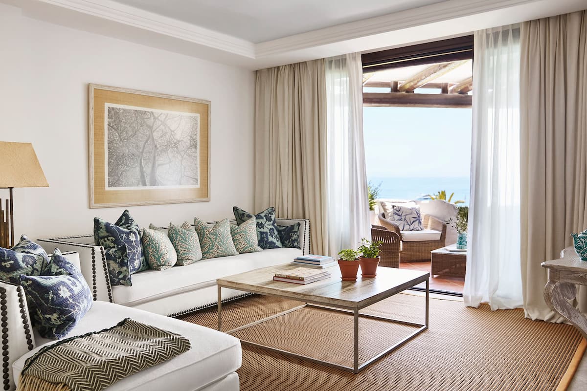 A modern living room with a sofa, coffee table, and a view of the ocean through large windows.