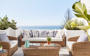Relax in a serene outdoor space with a wicker sofa and a view of the sea.
