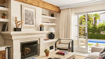 A living room with a fireplace, books, a coffee table, and a view of the outdoors.