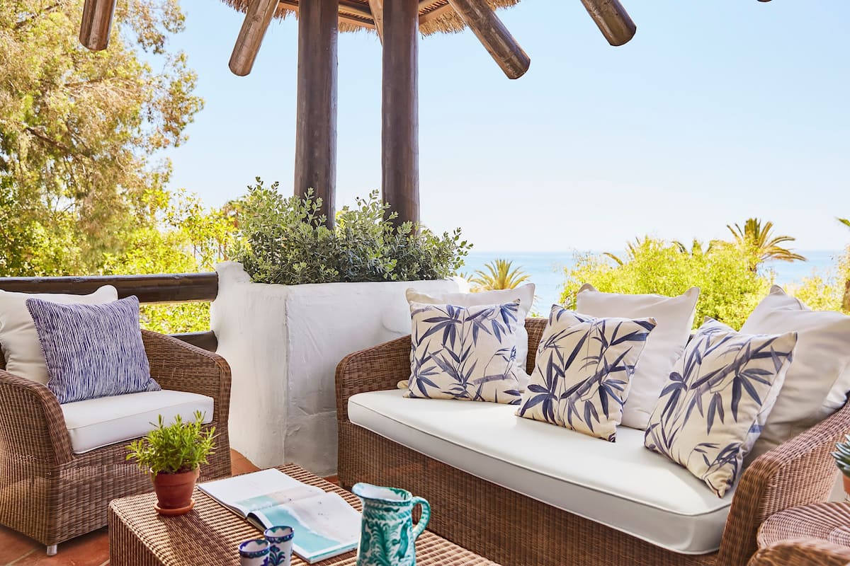 A wicker sofa with white cushions and blue floral patterns, a potted plant, and a book on a woven table.