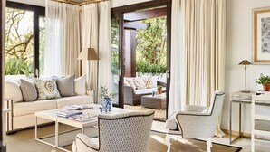 A well-lit living room with a sofa, armchairs, a coffee table, and a dining table. There is a view of greenery through large windows and a door leading outside. - Marbella Club Hotel Golf Resort & Spa (Marbella)