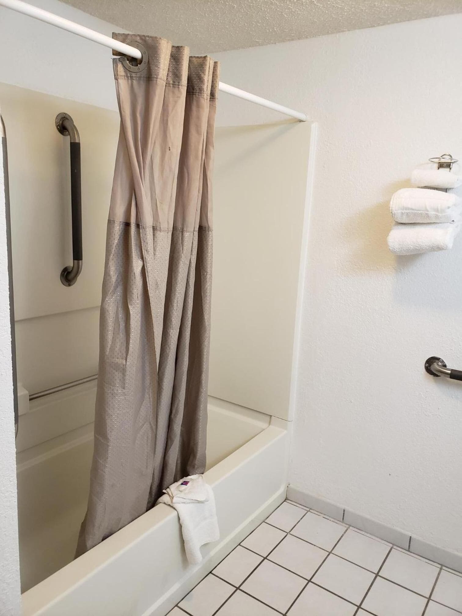 A shower area with a beige shower curtain, a white bathtub, and a towel rack with towels.