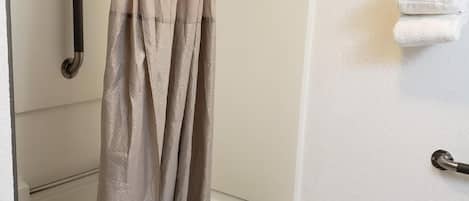 A shower area with a beige shower curtain, a white bathtub, and a towel rack with towels.