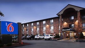 Un motel con un letrero que dice '6', un arco de bienvenida y varios autos estacionados.