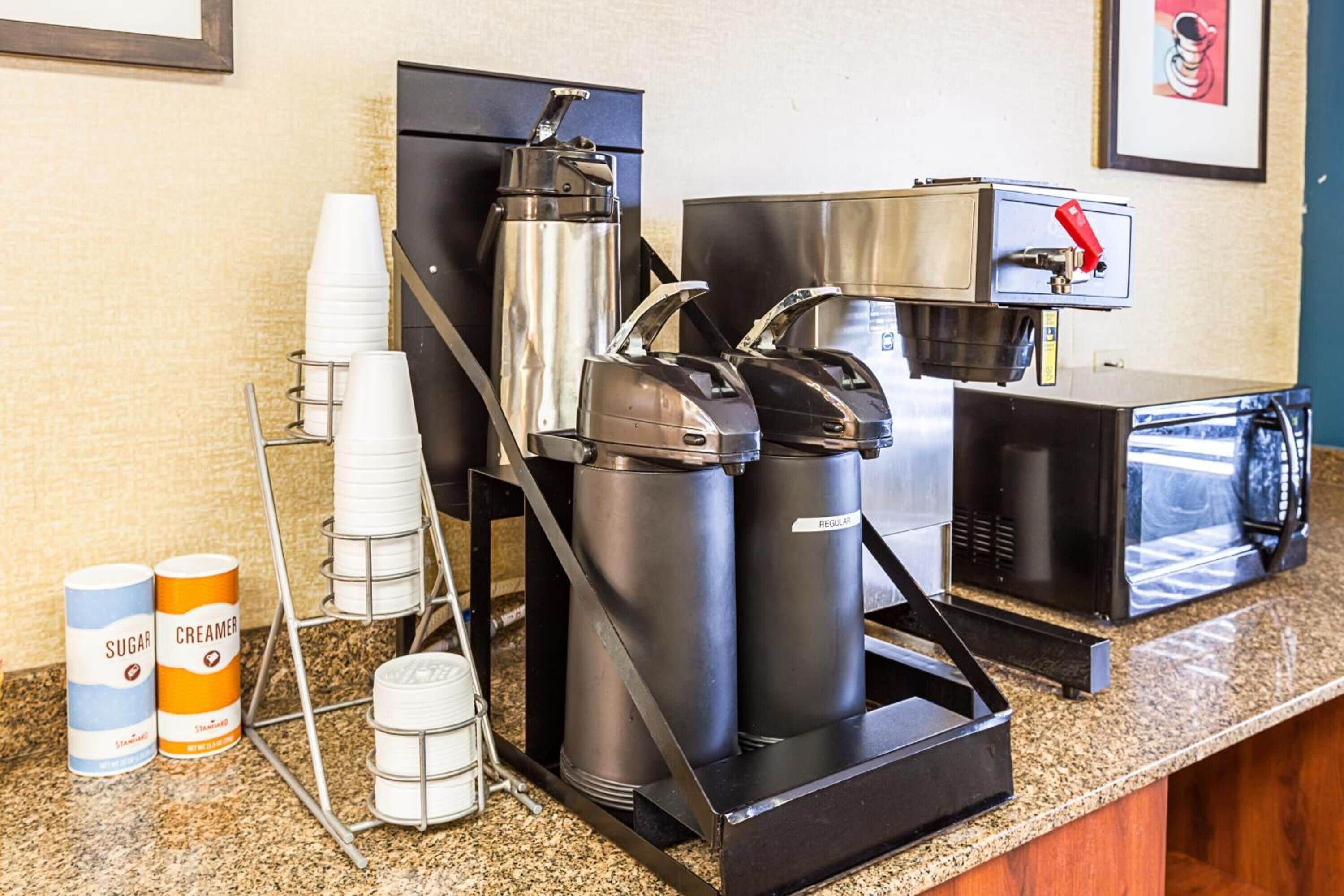 A coffee station with a coffee machine, milk frother, and sugar and creamer dispensers.