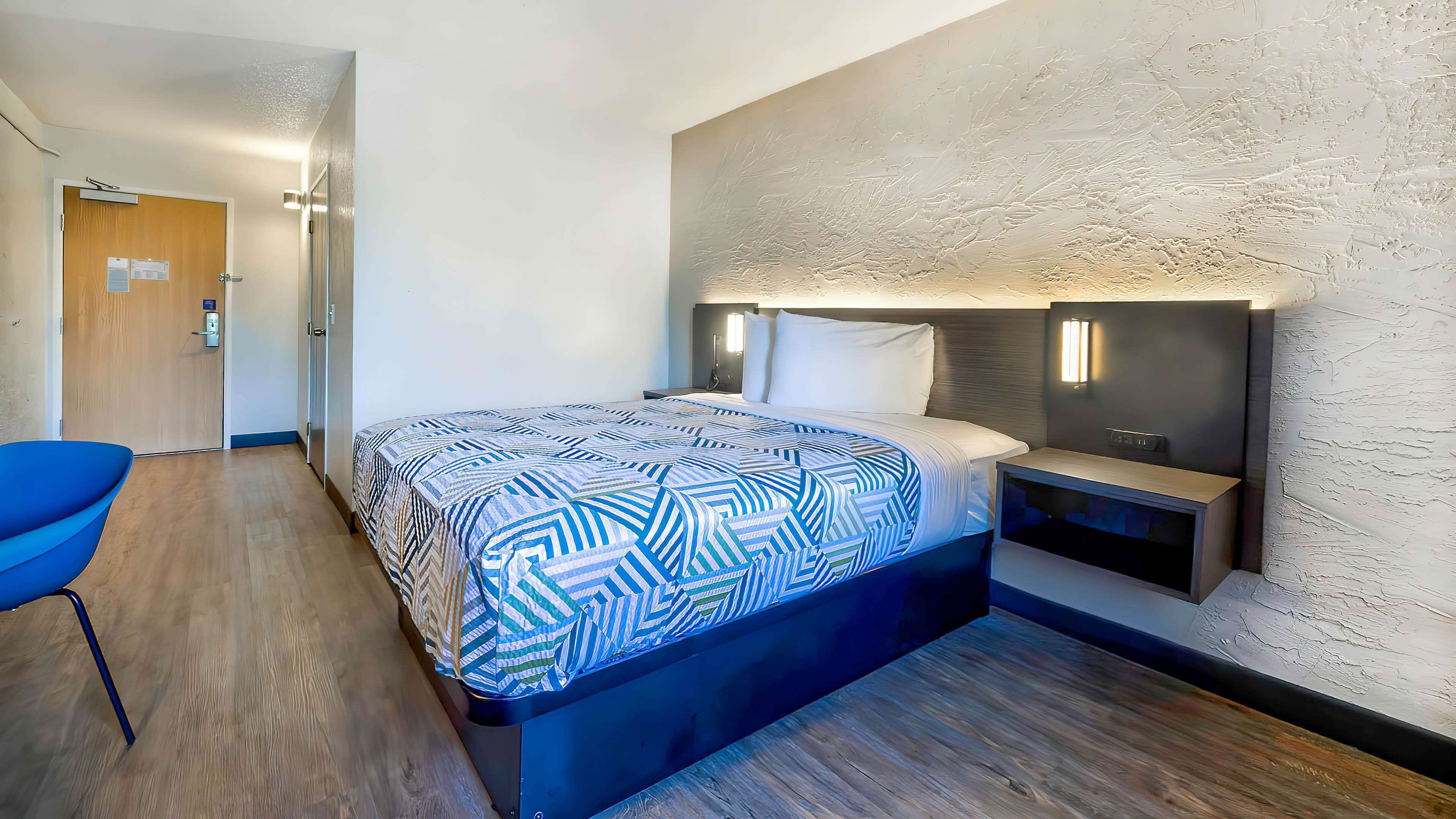 Habitació d'hotel moderna amb un llit gran, una taula de nit, una cadira i una paret amb relleu.